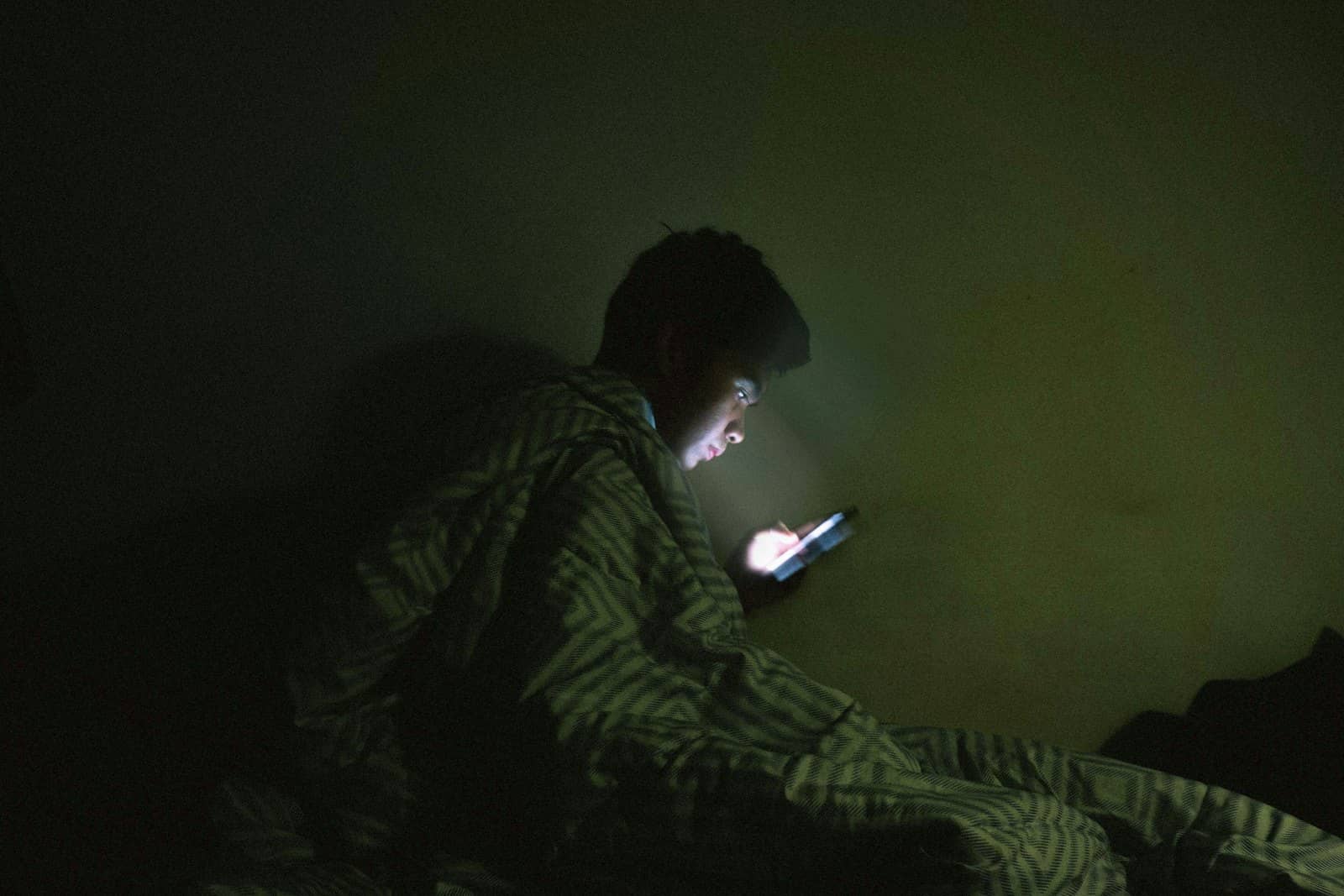 Someone scrolling a phone in bed in the dark